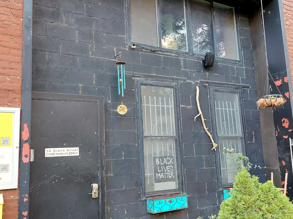 A sidewalk view of the dance studio CAVE with a microphone and speaker mounted on a second-floor window. A windchime is not far from the microphone.